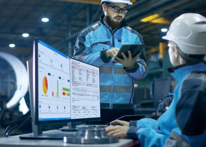 Two people in blue hard hats collaborating over the DRIVE NDT software displayed on a computer screen.