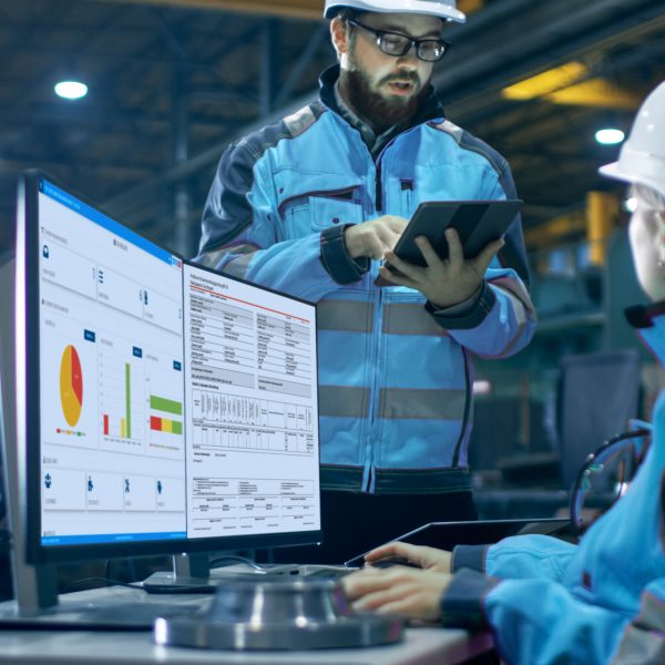 Two people in blue hard hats collaborating over the DRIVE NDT software displayed on a computer screen.